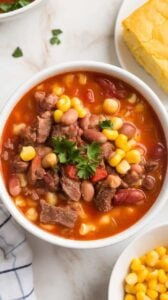 Top-down image of a bowl of Easy Cowboy Soup served on a white marble counter. This hearty soup is packed with ground beef, beans, potatoes, and corn in a rich, smoky broth. Garnished with fresh parsley and served with a side of cornbread, it's a warm and comforting meal that's perfect for a cozy night in.