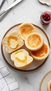 Top-down image of homemade Air Fryer English Muffins sliced open, showing a soft, airy texture. The muffins are golden brown, with butter melting on top, and served with jam and honey for a delicious breakfast.
