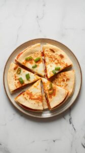 Top-down image of crispy Air Fryer Pizza Quesadilla sliced on a plate. The tortilla is golden brown, with melted cheese and pepperoni inside.
