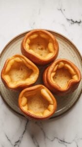 Top-down image of crispy Air Fryer Yorkshire Pudding served on a plate. The puddings are golden brown with airy centers.