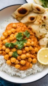 A photo of a steaming bowl of chickpea curry garnished with fresh cilantro and served over fluffy basmati rice. The rich, creamy sauce coats the chickpeas, and a squeeze of lemon adds a bright finish. A piece of naan bread rests on the side, ready for dipping.