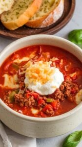 A bowl of slow cooker lasagna soup topped with ricotta, mozzarella, and parmesan cheese, served with garlic bread for a complete Italian-inspired meal.