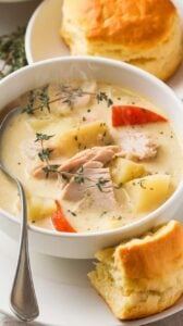 A warm bowl of creamy soup filled with tender turkey, hearty vegetables, and potatoes, served with a golden biscuit on the side for a comforting meal.